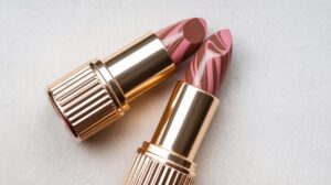 A photo of a golden lipstick with a pink and brown swirl pattern. The lipstick is placed on a white background. The lipstick is slightly open, revealing the pink and brown swirl pattern inside. There is a silver cap on the top of the lipstick.