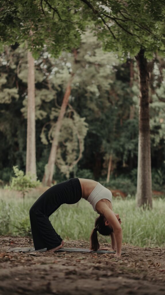 A photo of a yogi in a serene outdoor setting. The yogi is in a deep backbend pose, with her hands on the ground and her head touching the ground behind her. She is wearing a white top and black yoga pants. The background is a lush green forest with tall trees. The ground is covered with leaves. The lighting is soft.