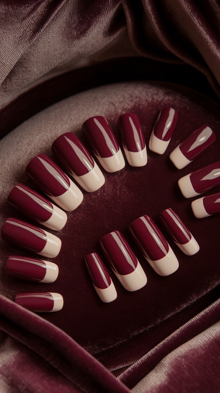 A set of burgundy and cream color block nails displayed on a soft velvet background