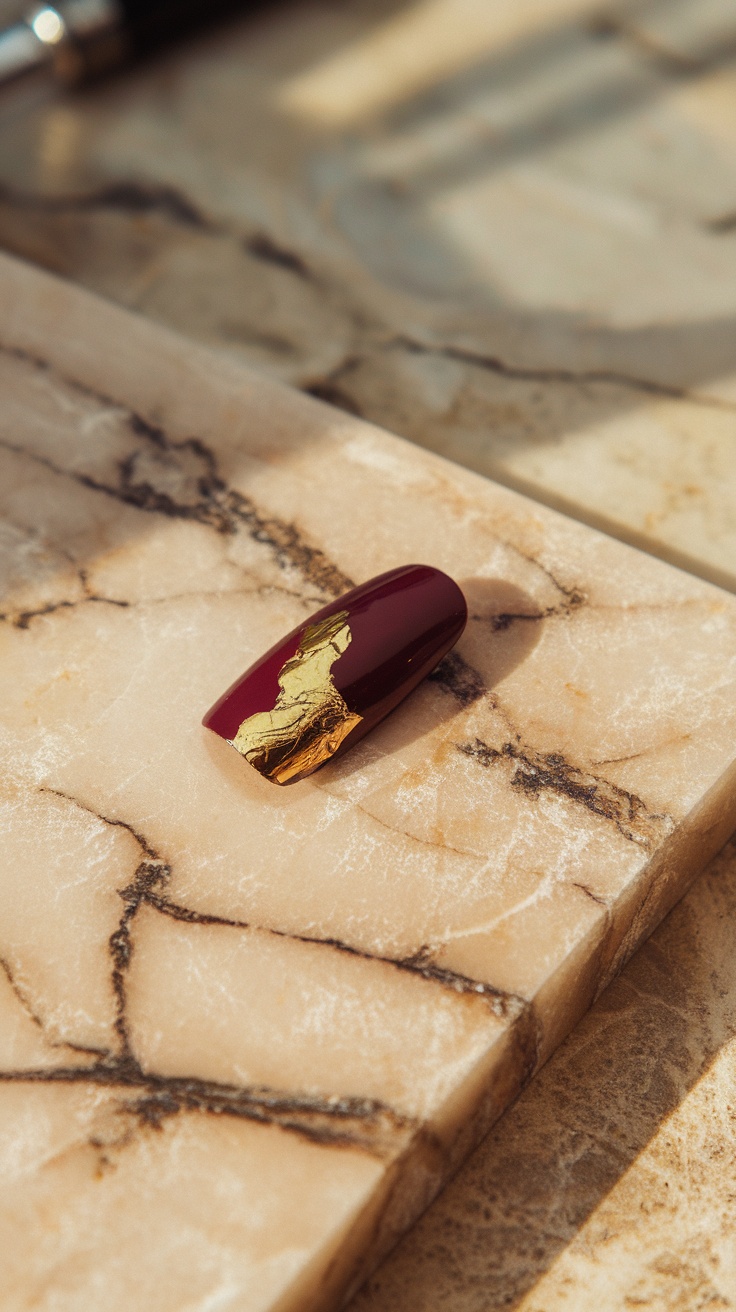 Wine red nail with gold accent on a marble surface.