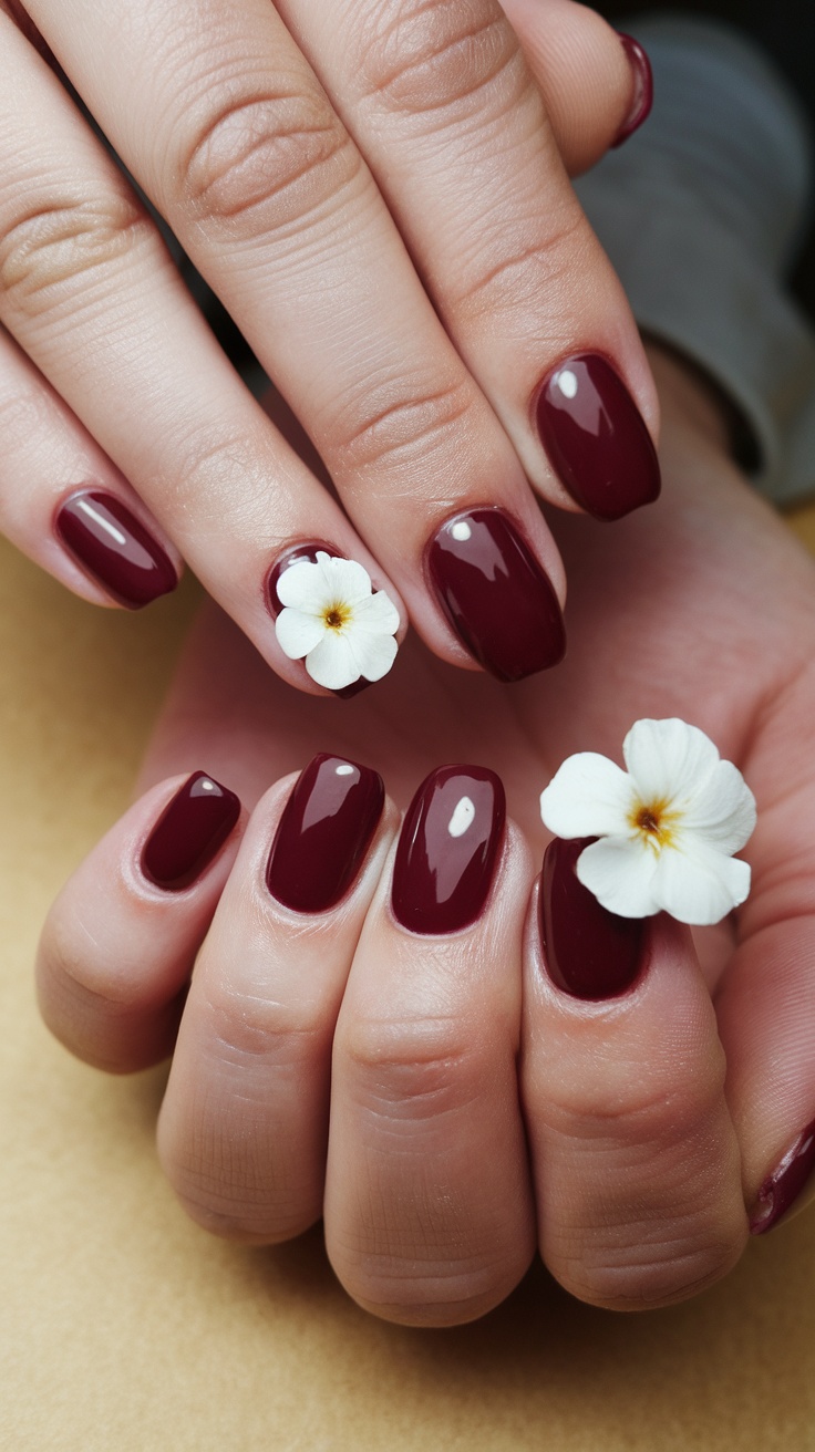 Close-up of hands with wine red nails featuring white floral accents.