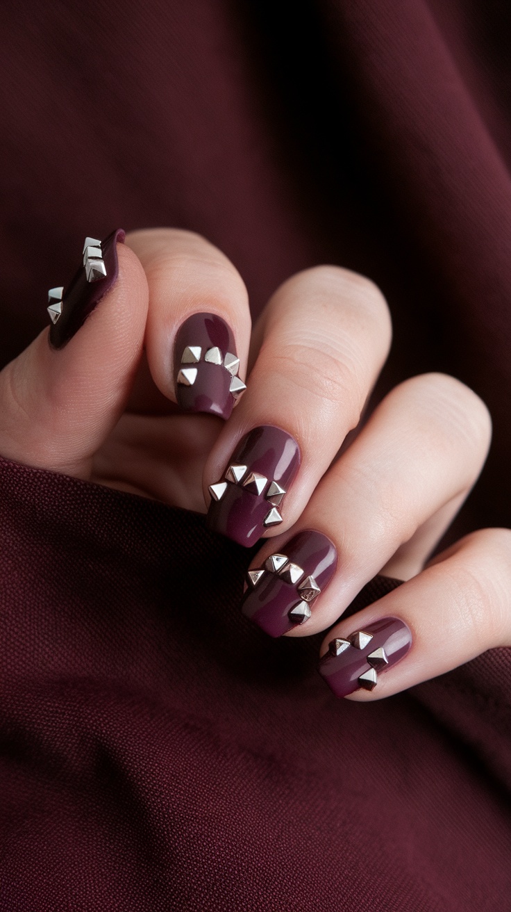 Vampy wine color nails with silver studs against a deep fabric background.