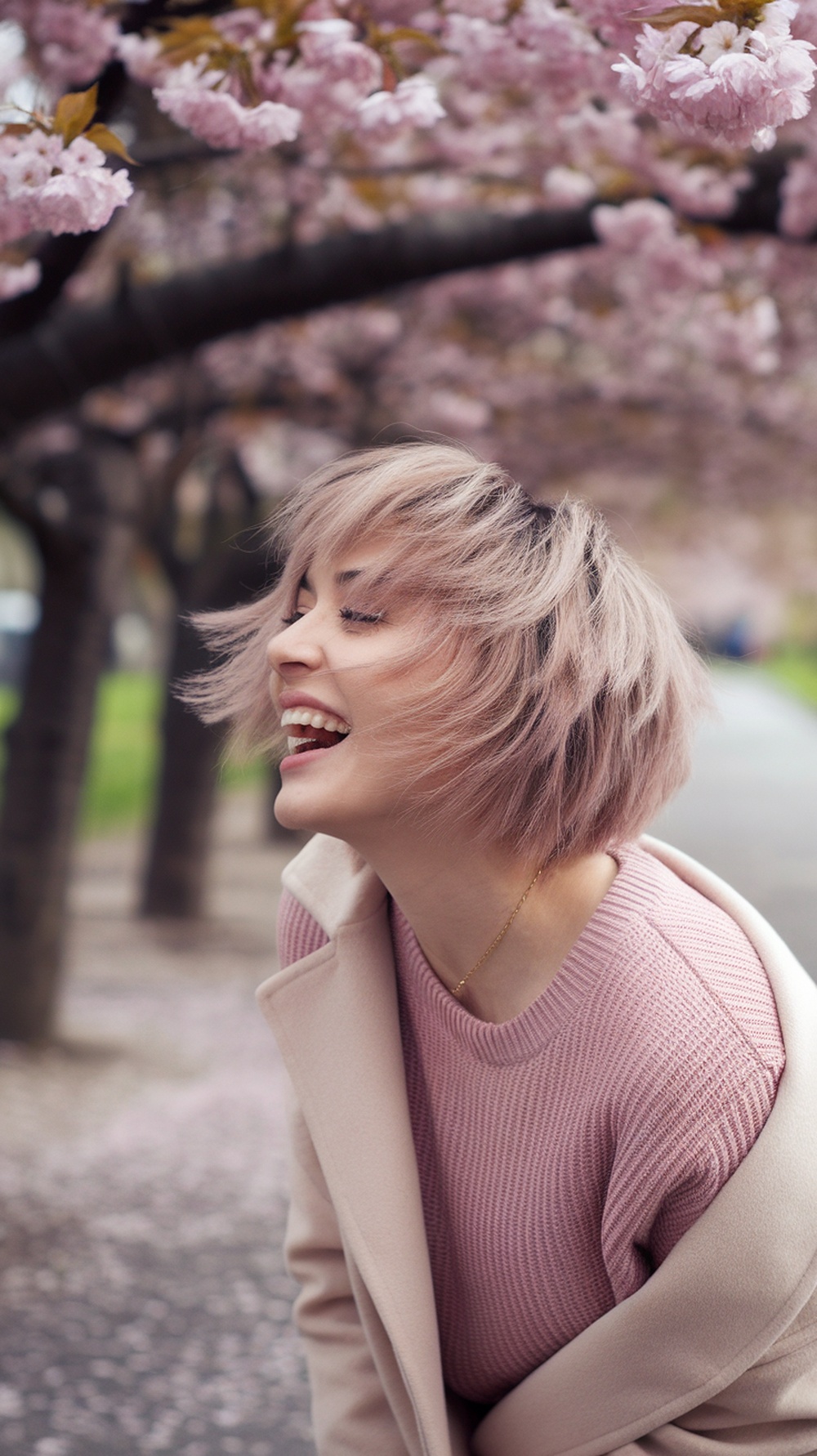 A woman with a playful layered haircut smiling under cherry blossom trees